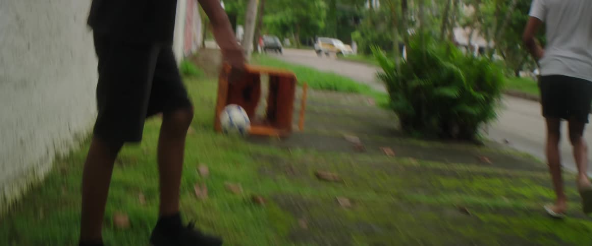 Teen boys with shorts t shirts and flip flop play football on the street next to road