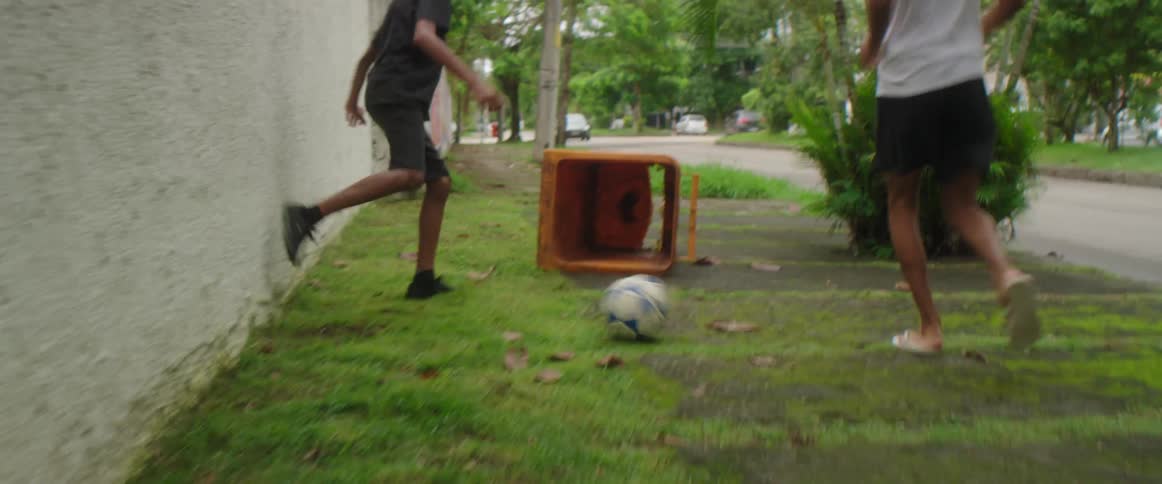 Two young friends playing with a soccer ball on the sidewalk near the road