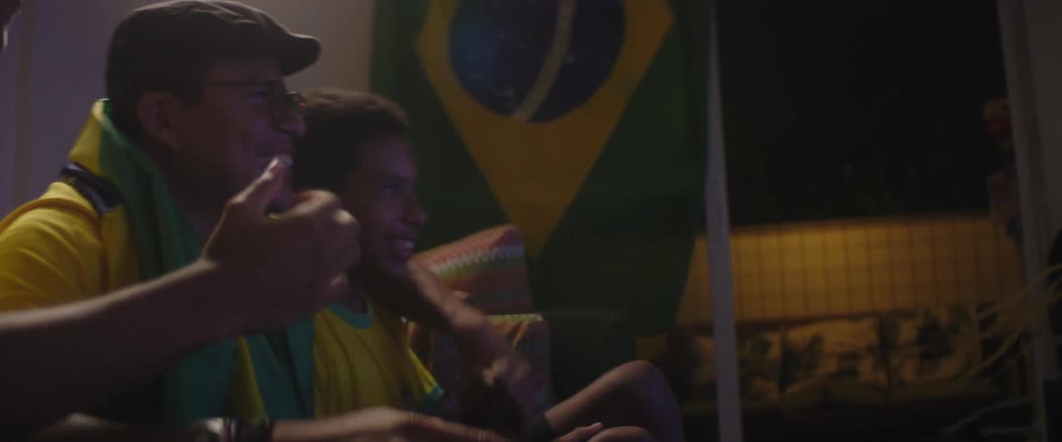 Father and son sitting on the living room celebrate while watching a game on television