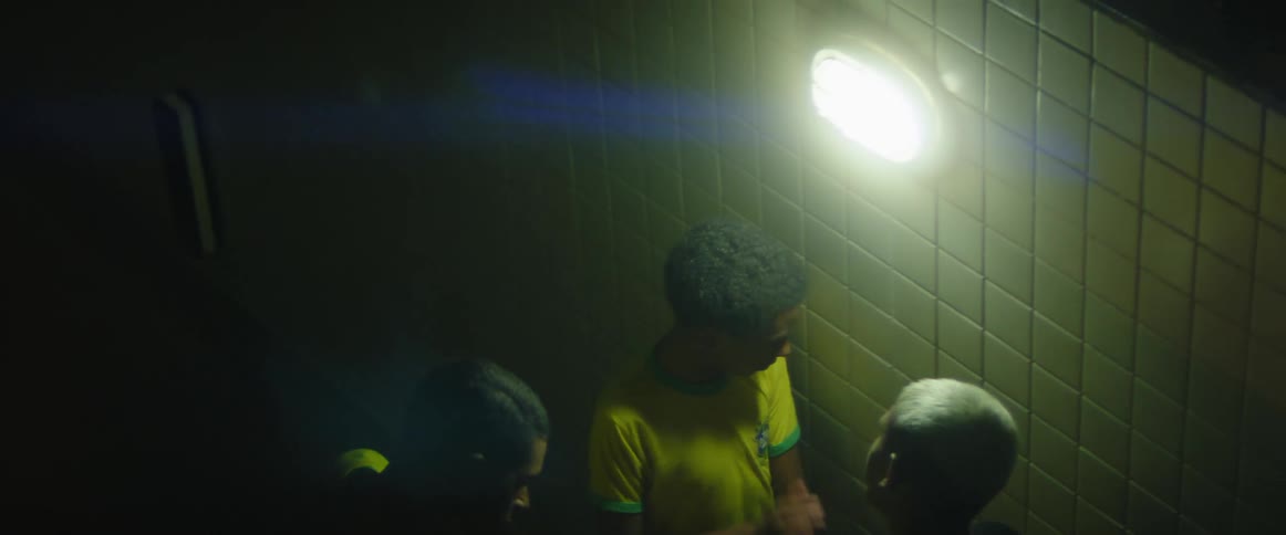 Three boys watch a game on a cell phone and then one runs his hands through his hair as another hit the wall