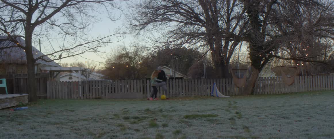 A girl kicks a soccer ball past her father as they play in their backyard