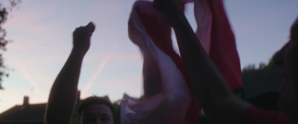 A group of men hold a flag and cheer and pump their fists in the air outside