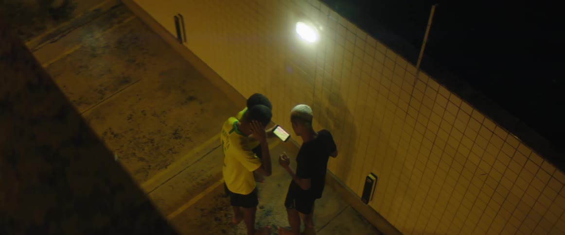 A group of youths watches football match on smartphone next to wall at night