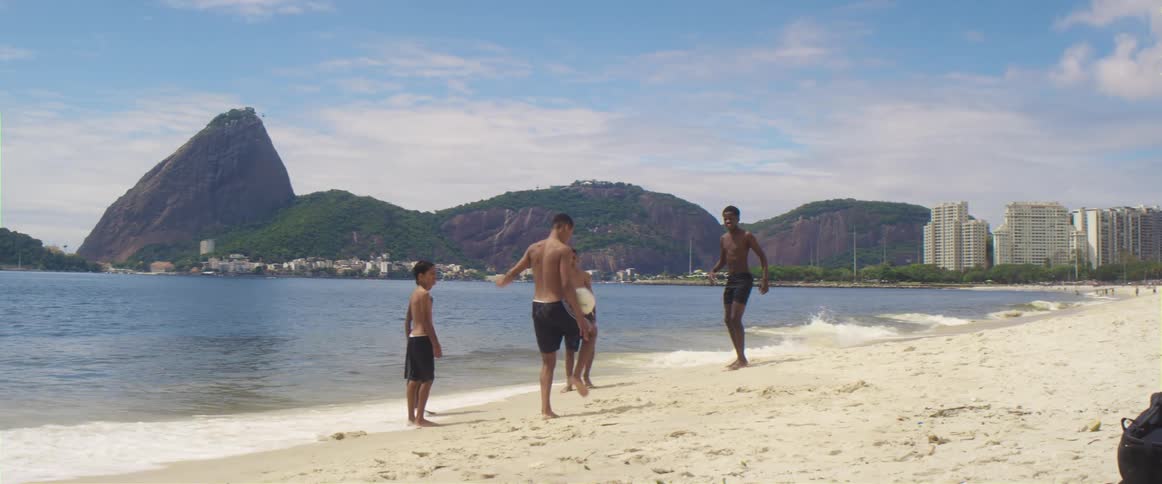 A group of youths plays football on the white sand beach next to sea