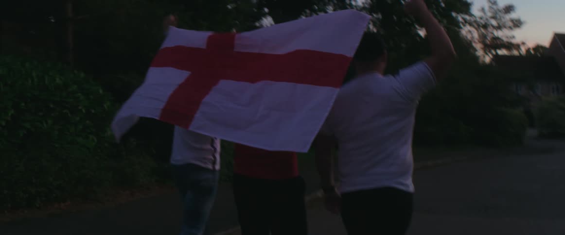 Three men walk outside together holding a flag behind them