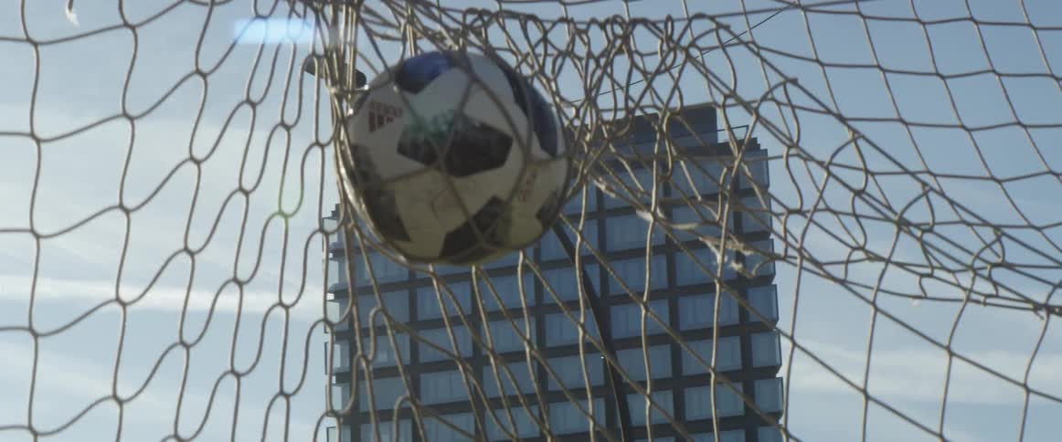 Soccer ball gets entangled on a goal net in a field near a building