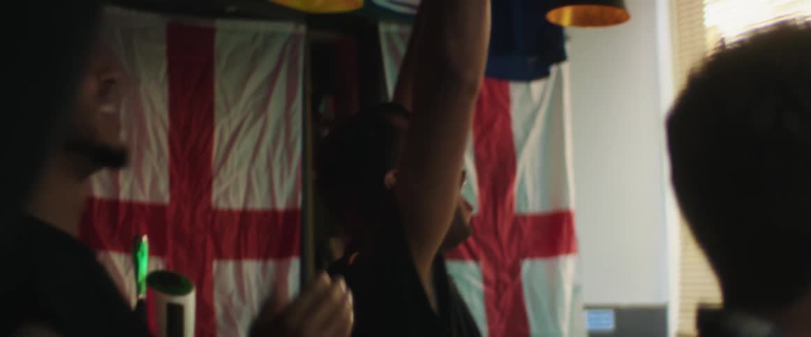 Friends celebrate while watching a game on a screen inside a bar