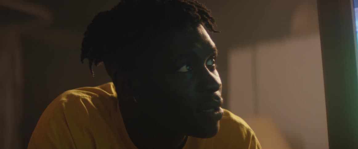 A man is sitting and watching a game intently in television when another man walks past