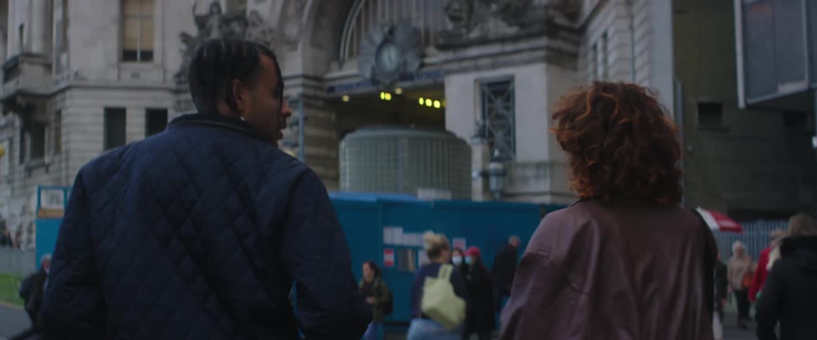 A man and woman chat while walking together through a city during the day