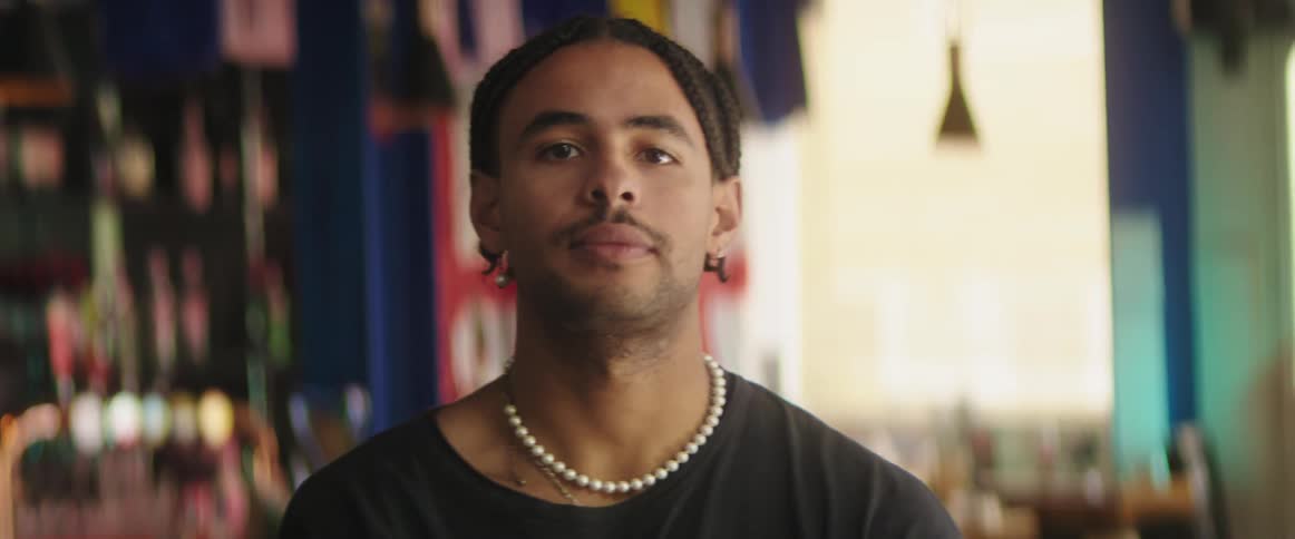 Man wearing necklace and earrings adjusts his hair braids