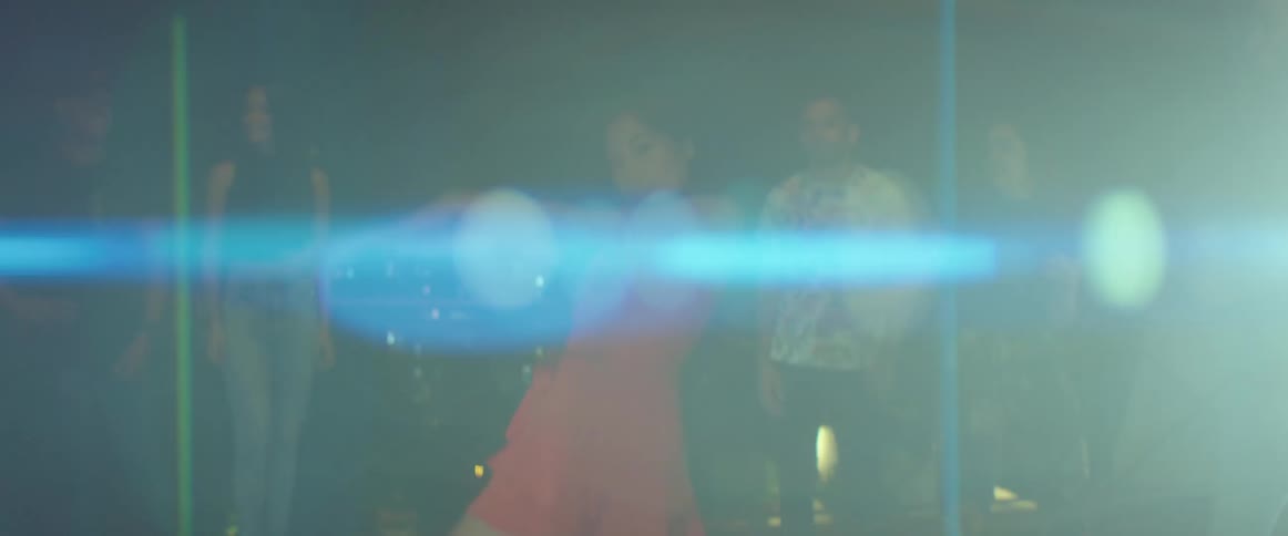 A woman looks into the camera as she dances on a rooftop in a city at night surrounding by a crowd