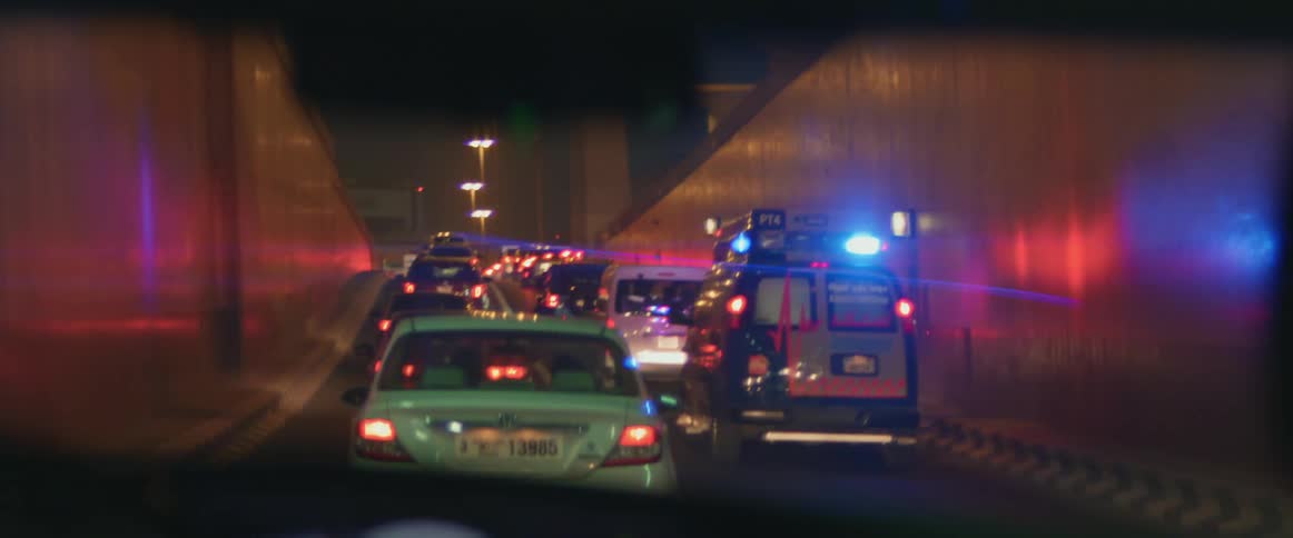Multiple vehicles drive in two lanes with ambulance lights flashing