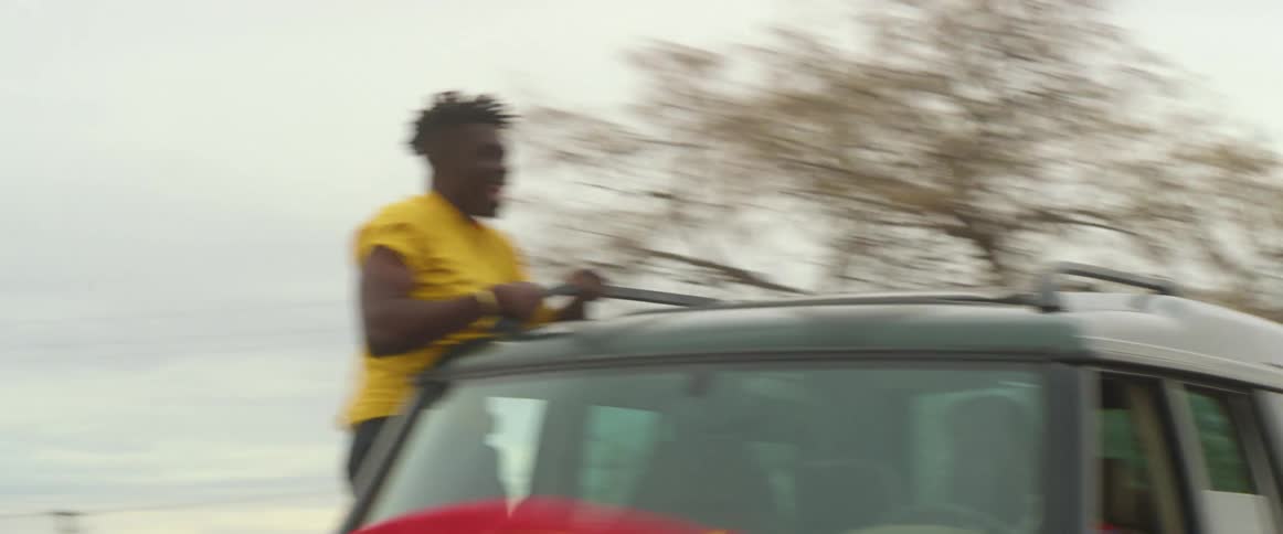 Man sitting on the window of a moving car with a waving flag over the hood