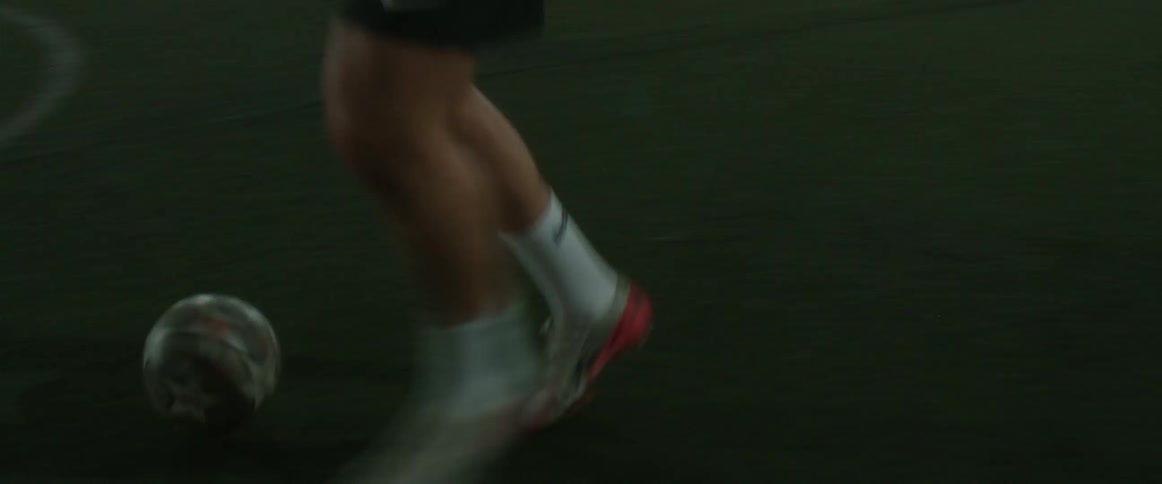 A male soccer player kicking around a ball on an outdoor field at night