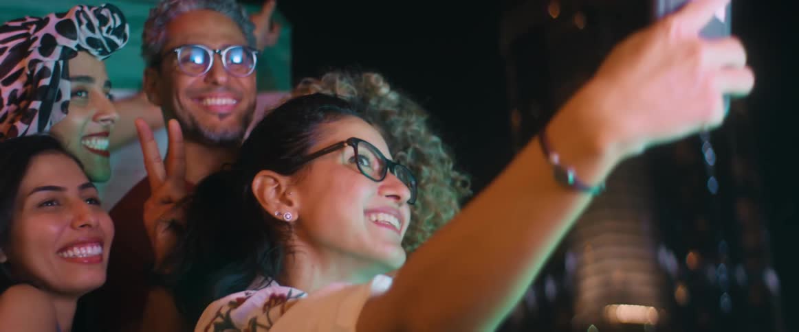 Group of happy friends take a selfie in front of a flag in the city at night