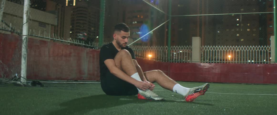 Hispanic man sitting down tying his cleats at night