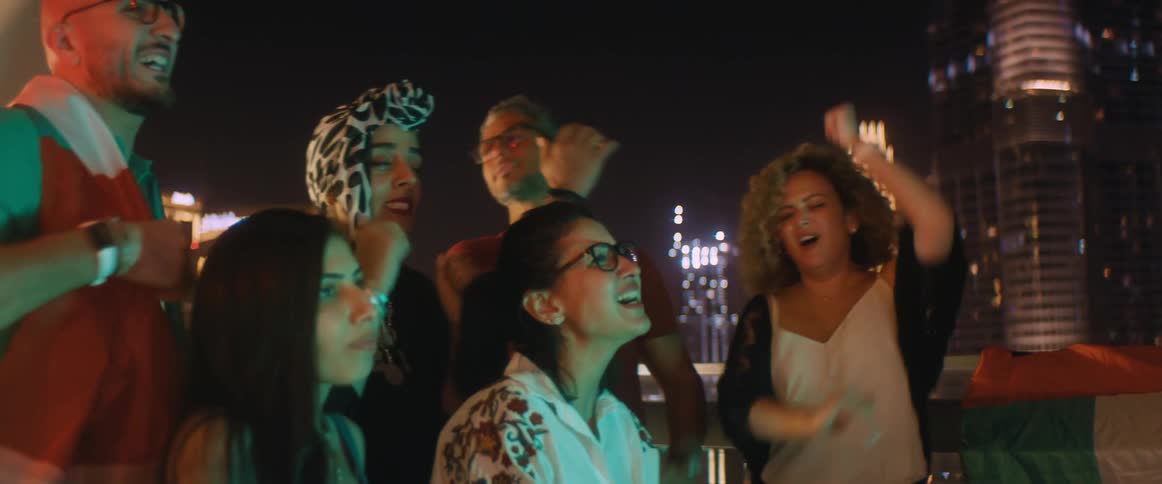 Group of excited friends watching a game on a television in the balcony at night