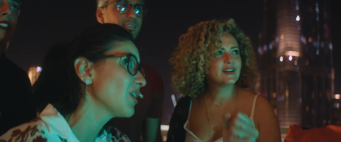 A group of people watching something on a roof top talk and then jump up and start cheering