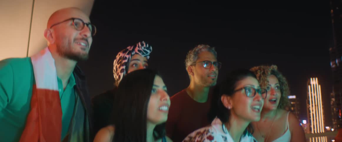 Friends sit watching broadcast before jumping and cheering with city skyscrapers in background