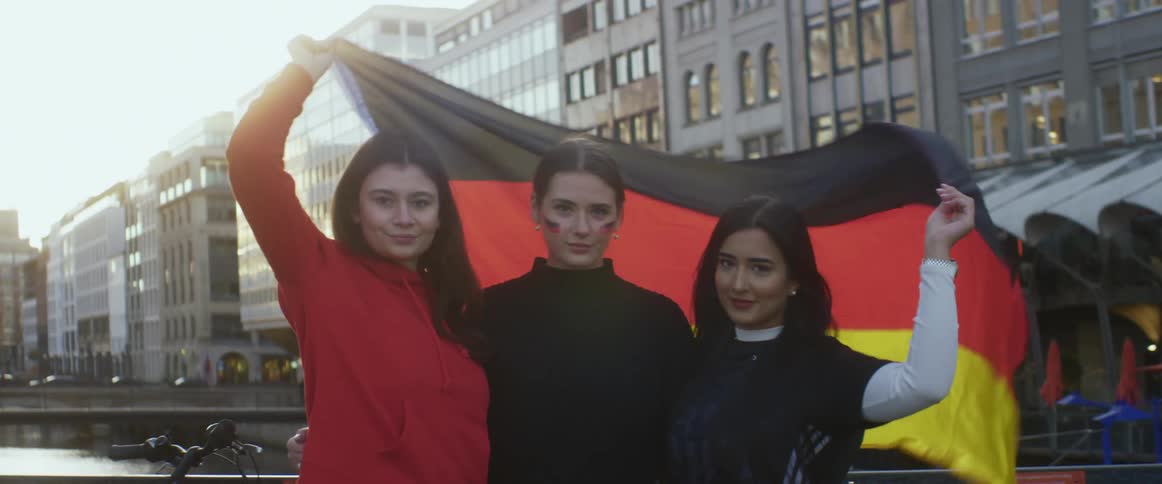 Three women hoist a flag over their heads as they pose on a bridge downtown