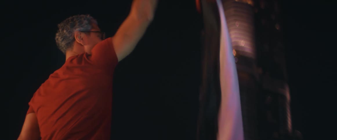 An excited man waving a flag and jumping near a tall skyscraper at night