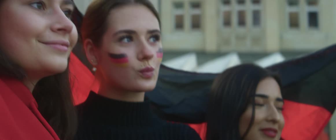 Three teenage girls smiling and laughing in front of a flag in a city