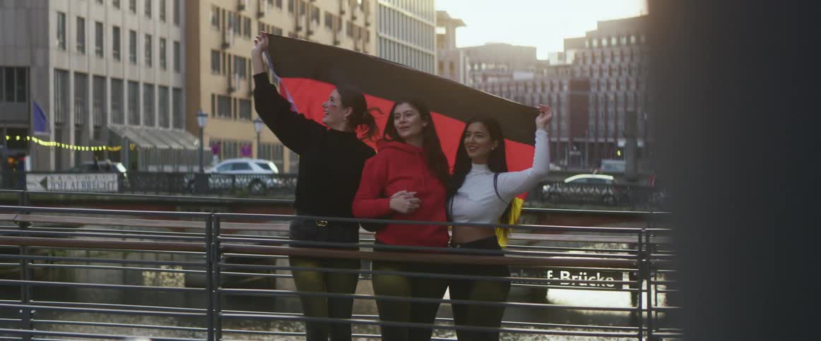 Friends waving a germany flag over a bridge in the city at morning