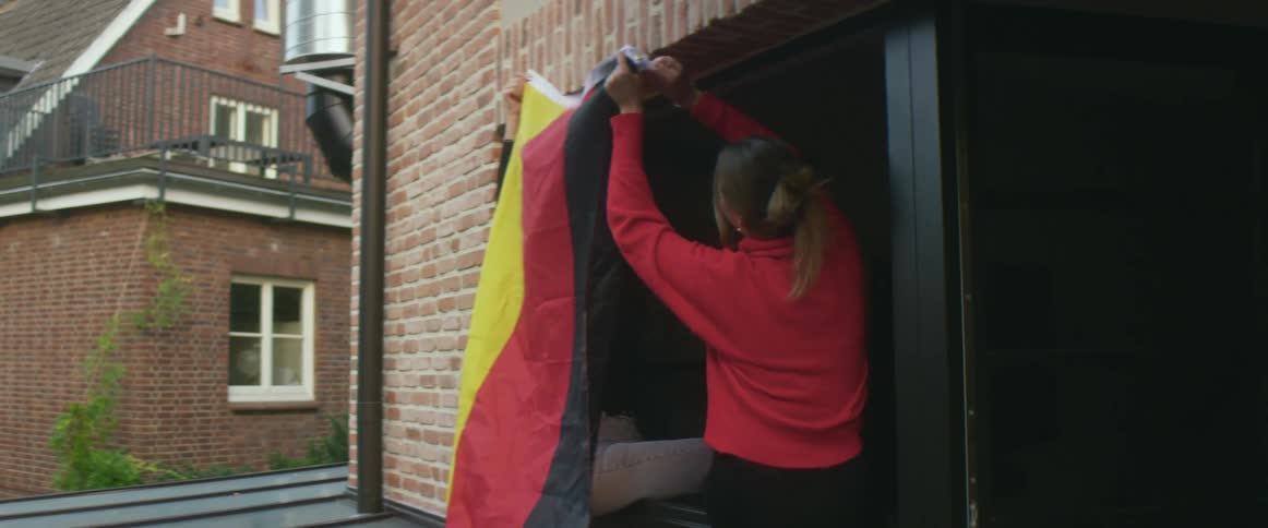 Two women laugh as they try to hang a flag in a garage entrance