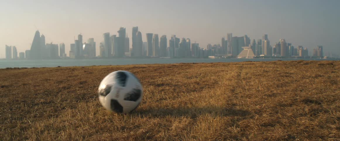 Soccer balls rolls across a field in front of a city skyline