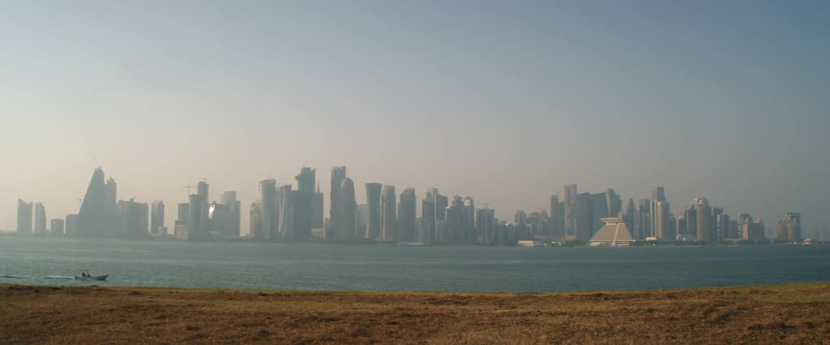 A boat travels down a river past the city skyline in the early morning