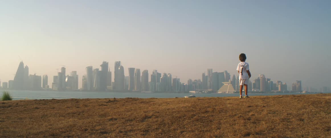 Boy standing on a hill looking at the waterfront city skyline at sunset