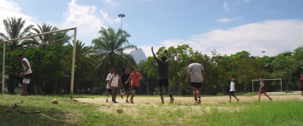 A group of boys play soccer and after one boy kicks the ball in the goal several boys cheer high five one another and dance
