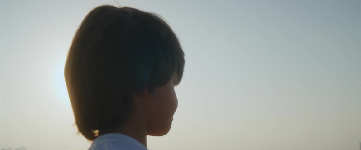 A young boy stands in front of the water and looks towards the city skyline