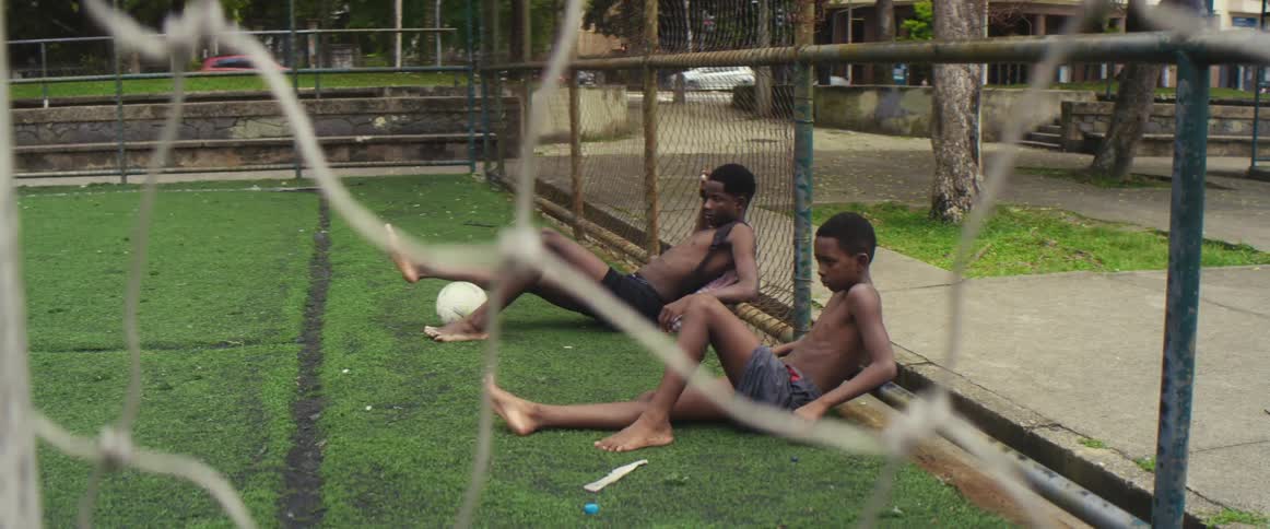 Youths recline on soccer field as traffic passes along roads in background