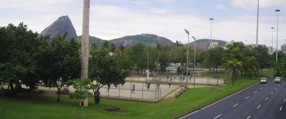 Men playing basketball on an outdoor court near a busy road