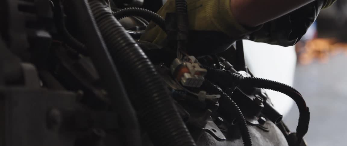 Mechanic wearing gloves disconnects cables from an engine inside an autoshop