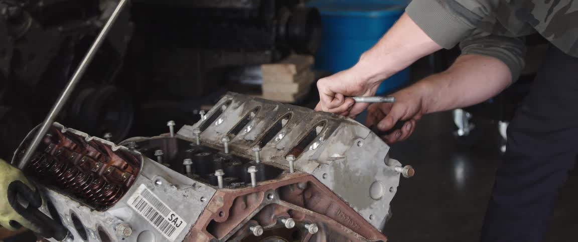 Two mechanics remove bolts on an engine