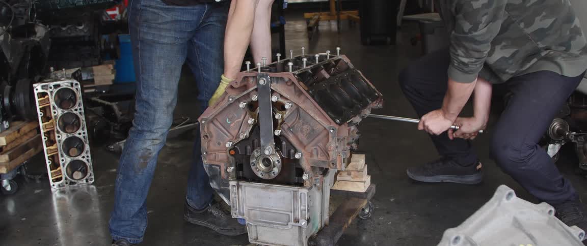 Two men are working on an engine with one using a wrench to turn a bolt