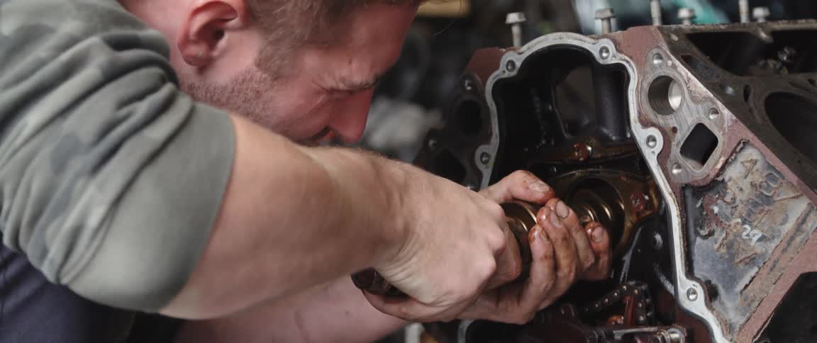 A man is working on a car engine and using a tool