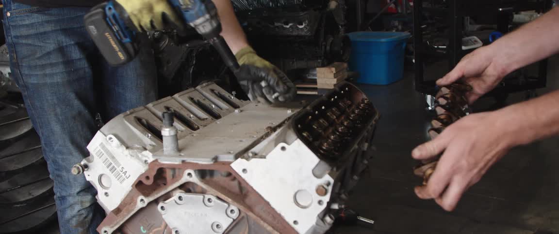Mechanics disassembling an engine using power tools inside a warehouse