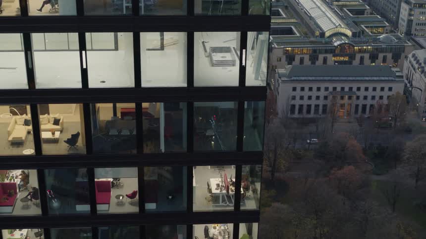 People sit and stand in offices in building as traffic passes by on the street