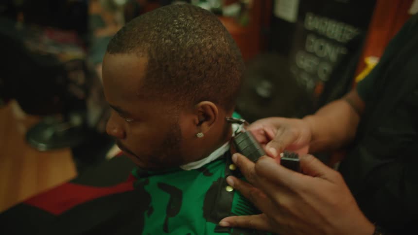 Bald barber with beard black t shirt and vest cuts mans hair with clippers in barbers shop