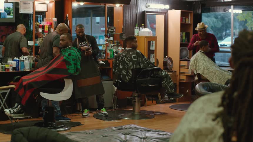 Barbers working on the haircuts of several clients sitting in the barber shop