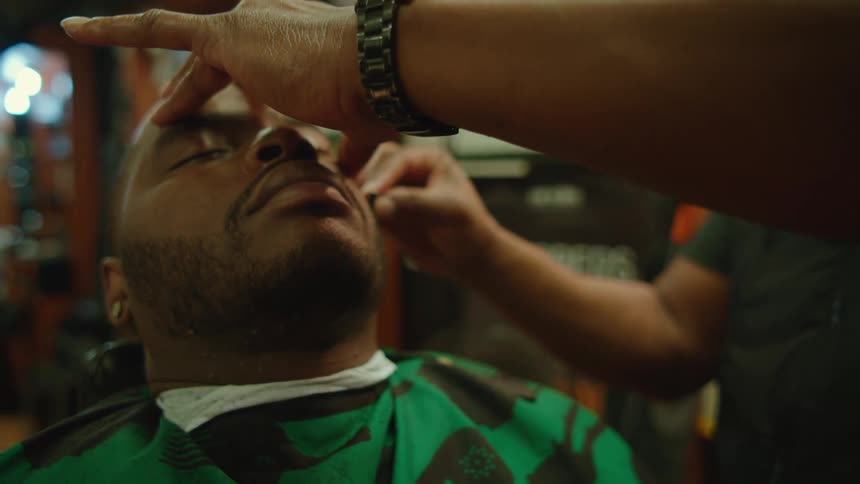 Man sits with his eyes closed as barber shapes his beard
