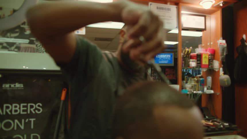 A barber uses a pair of scissors to trim the hair of a customer in a barber shop
