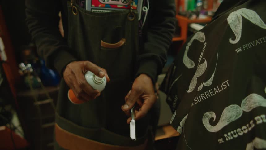 Barber applying spray on a razor behind a client sitting on a chair in the barber shop