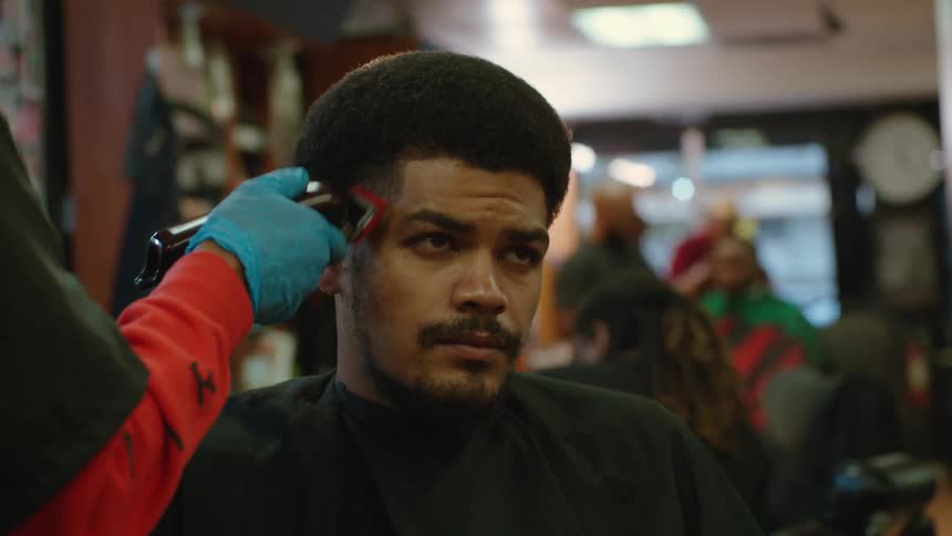 Man with black apron has his hair cut in barber shop