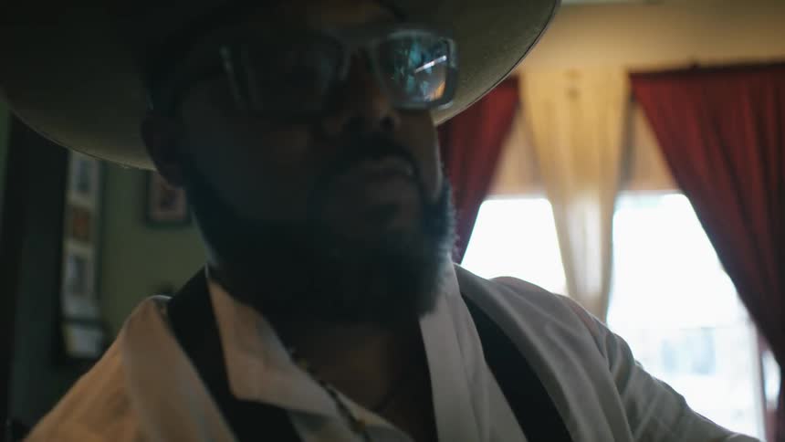 Barber with hat glasses beard white shirt and black apron cuts mans hair with scissors in barber shop
