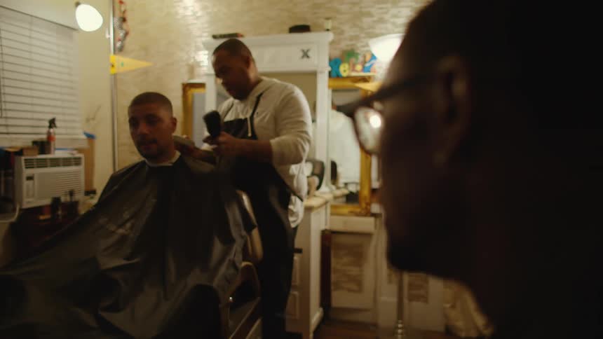 A man talks to a friend while he gets his hair cut by a barber