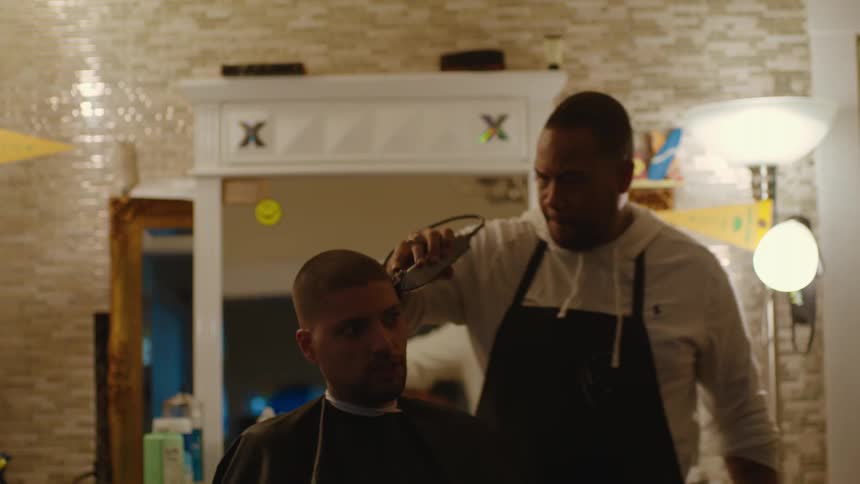 A barber uses an electric razor to cut a clients hair turning him as he cuts